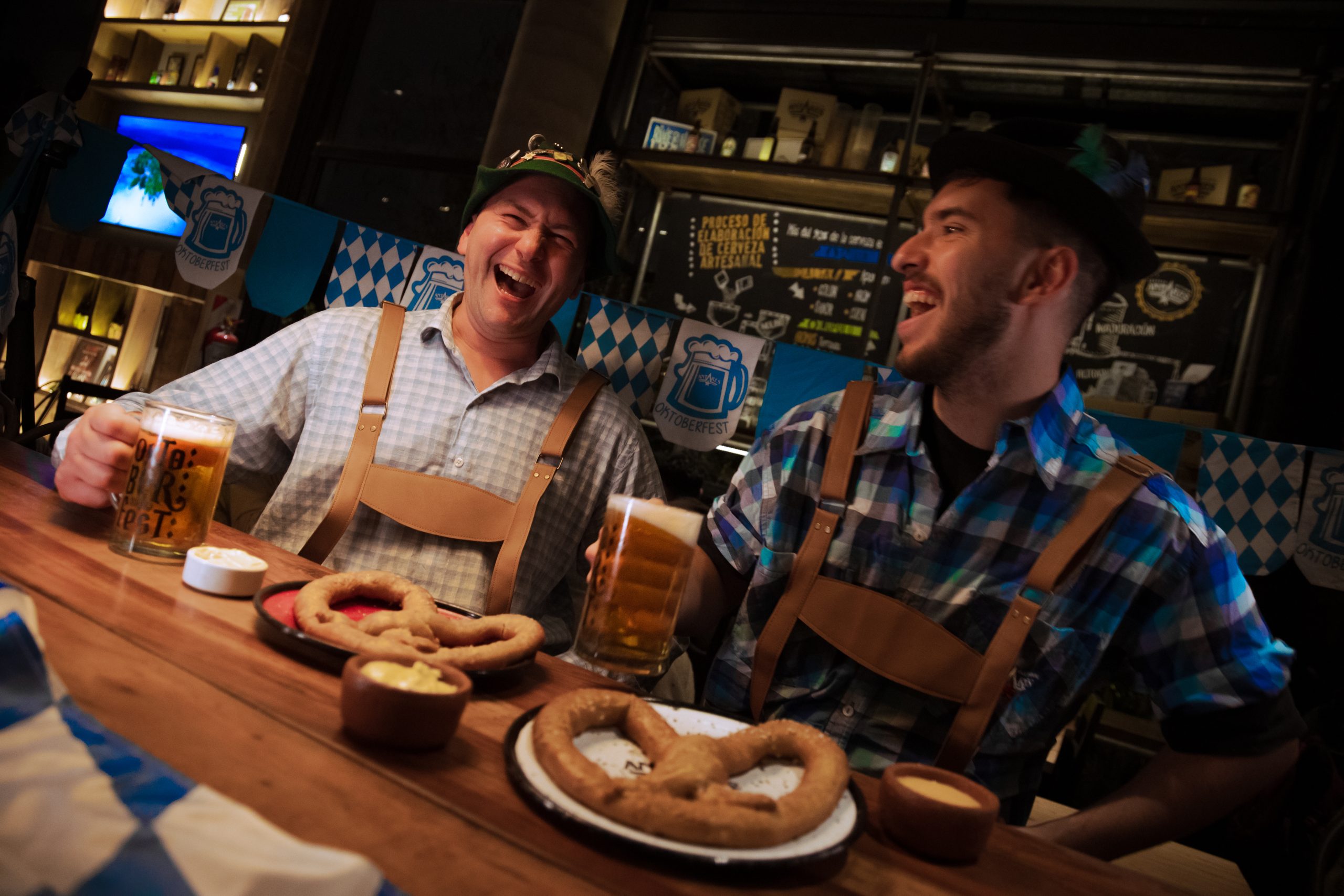 Dos hombres caracterizados de cerveceros alemanes están sentados a la mesa para comer pretzel con chopp de cerveza Lager, plato típico alemán.